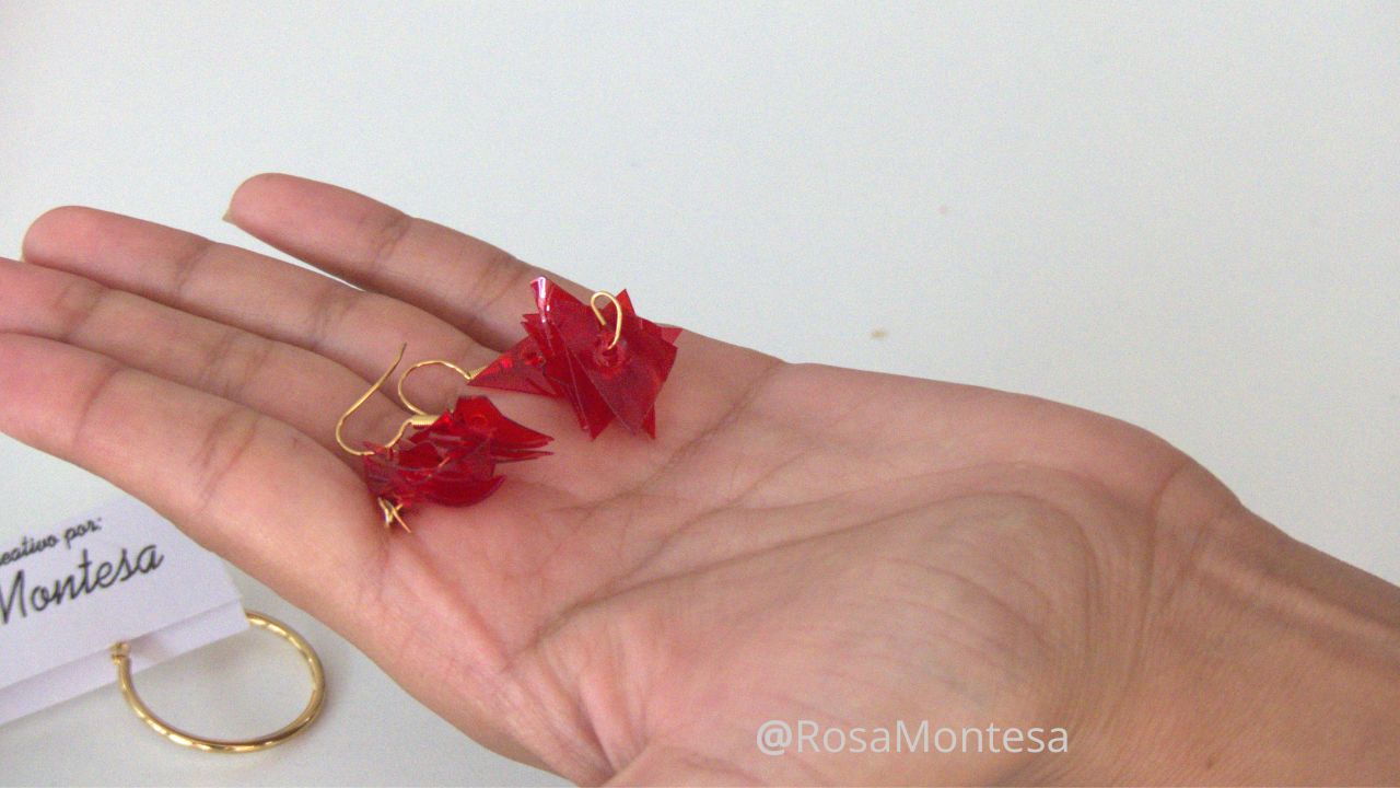 Manos de una niña en el taller de bisutería reciclando botellas de plástico. Pendientes rojos hechos por ella misma